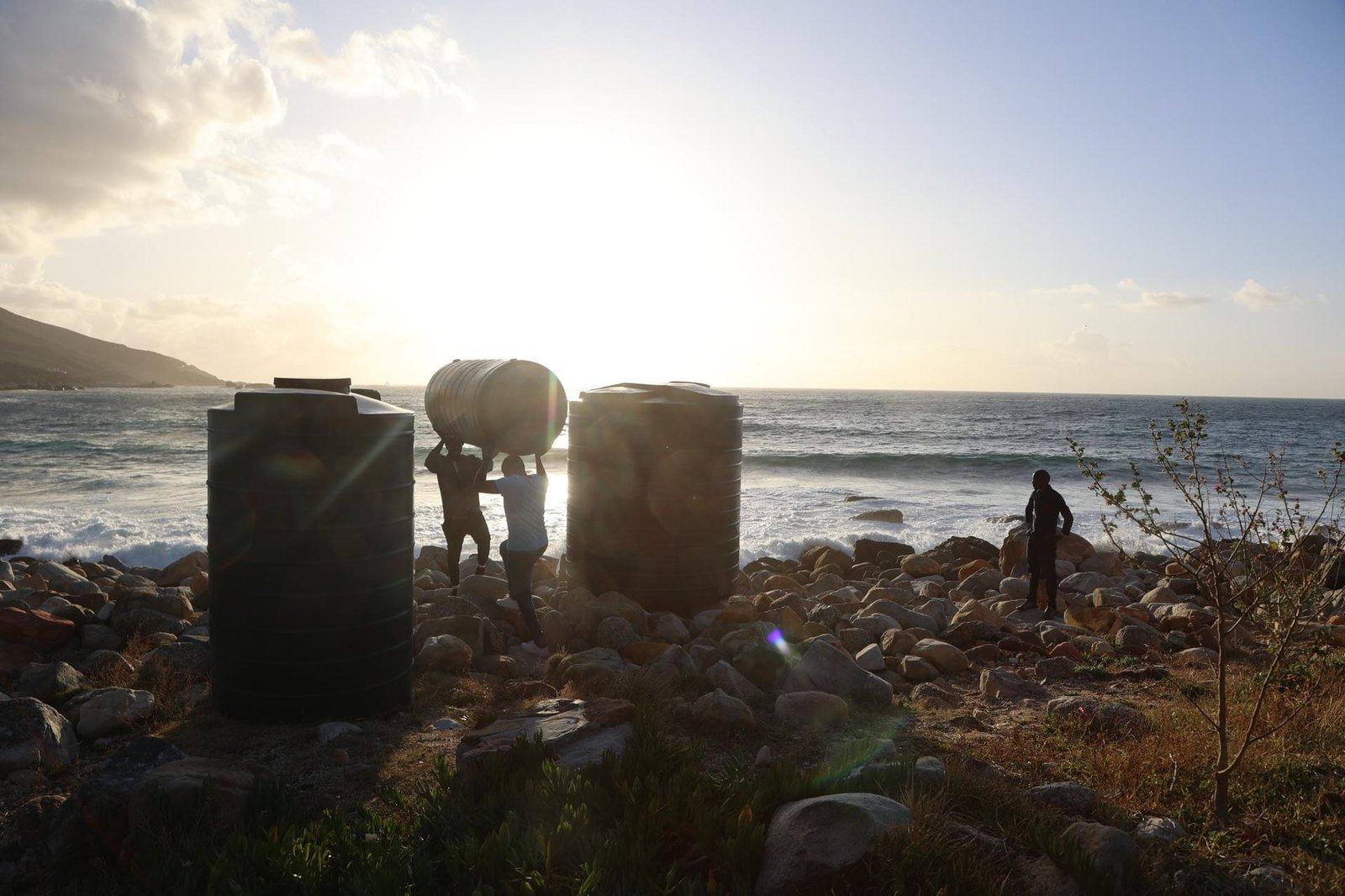People carrying Makulu tanks along the coast at sunset